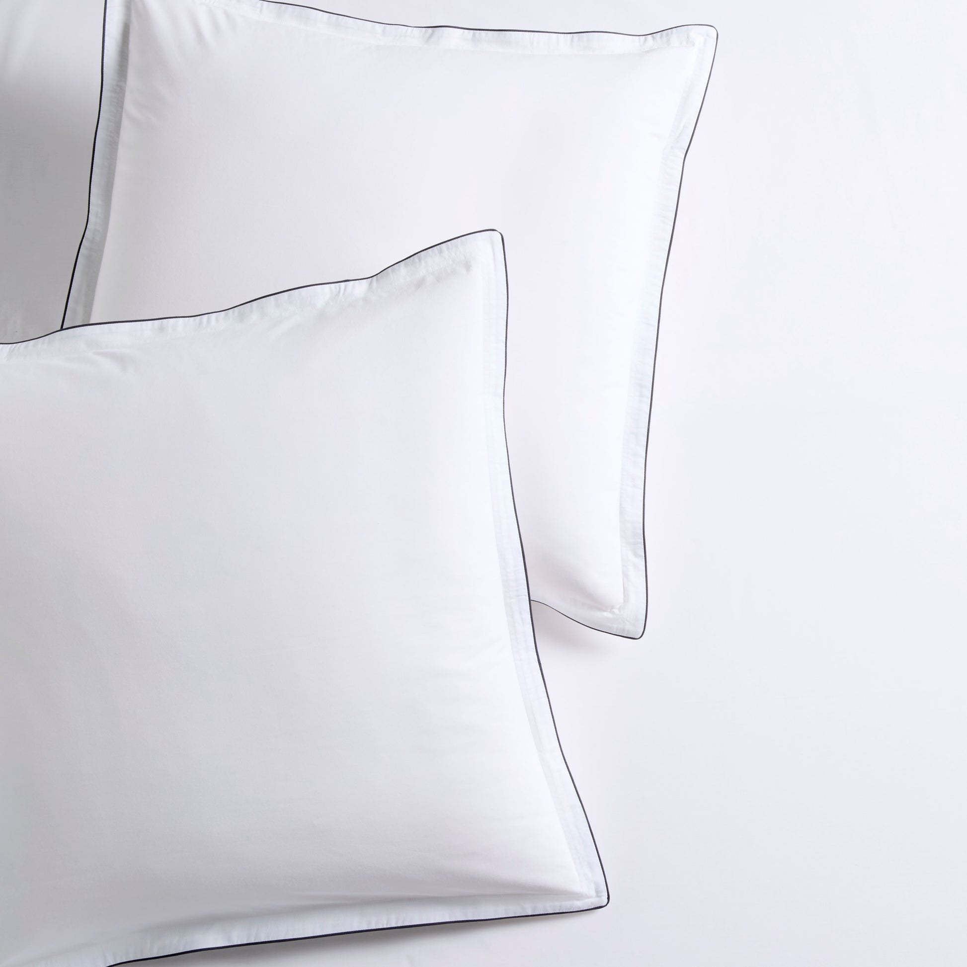 Set of two white percale Euro shams with navy piped edges and subtle double-stitch detailing.