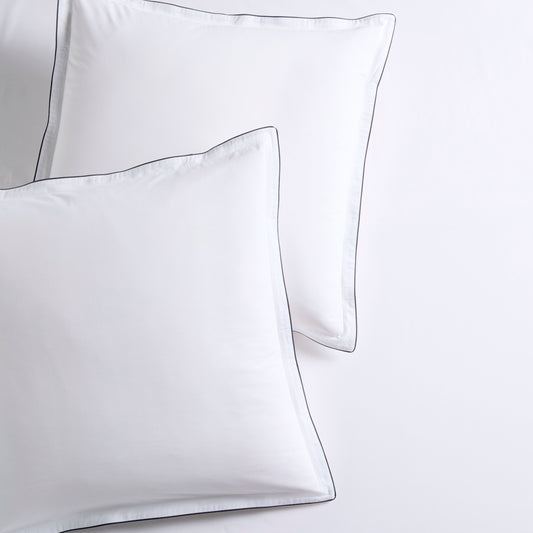 Set of two white percale Euro shams with navy piped edges and subtle double-stitch detailing.