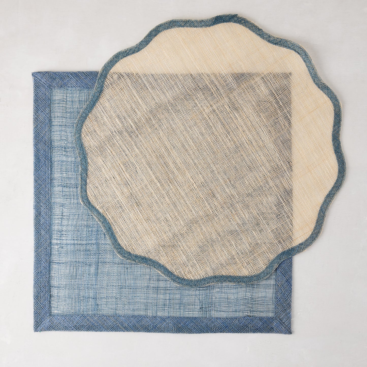 Natural abaca scalloped placemat with blue border over a rectangular blue placemat.