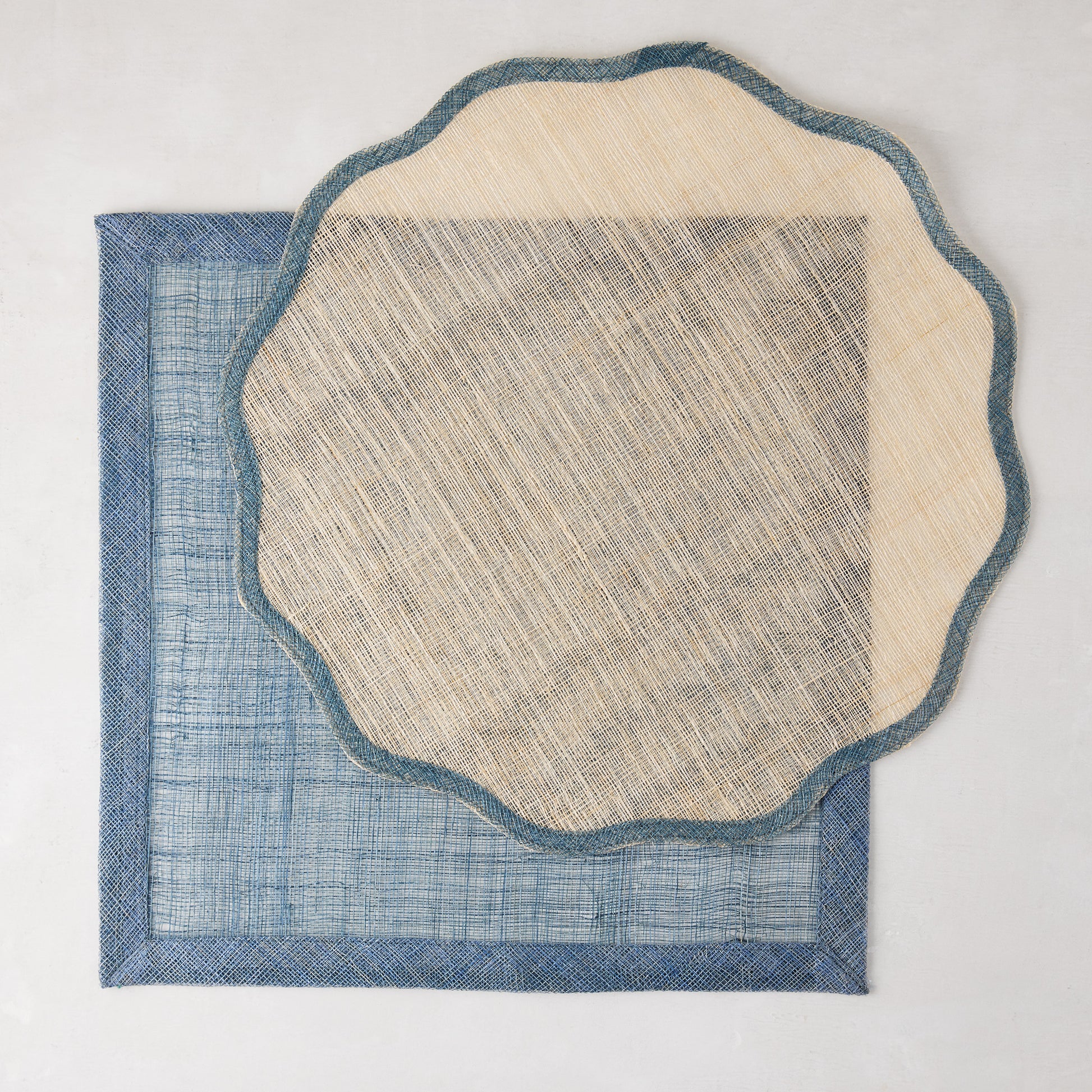 Natural abaca scalloped placemat with blue border over a rectangular blue placemat.