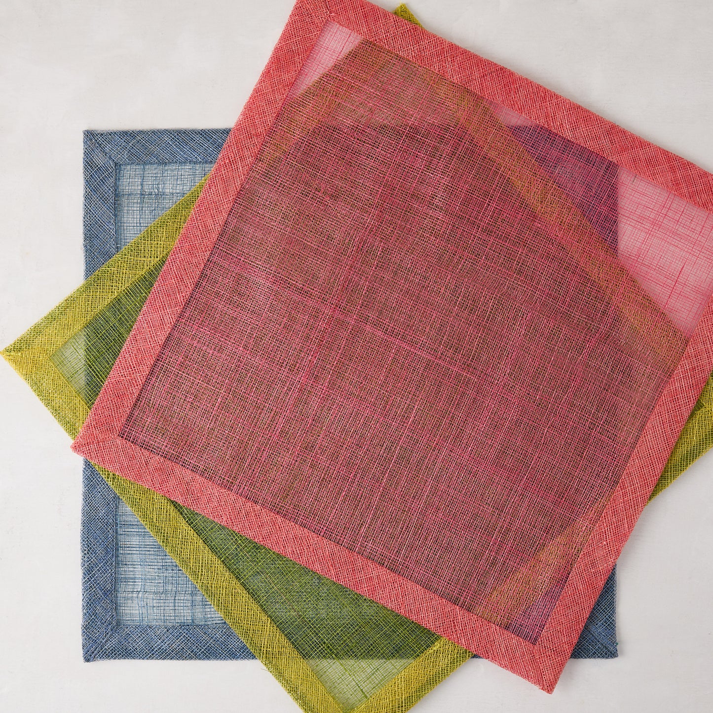 Newport Pink Square Abaca Placemat with dark pink border, layered over green and blue placemats.