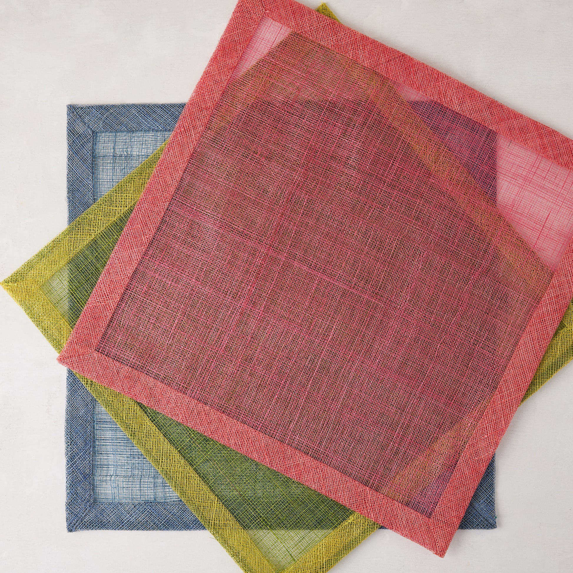 Newport Pink Square Abaca Placemat with dark pink border, layered over green and blue placemats.