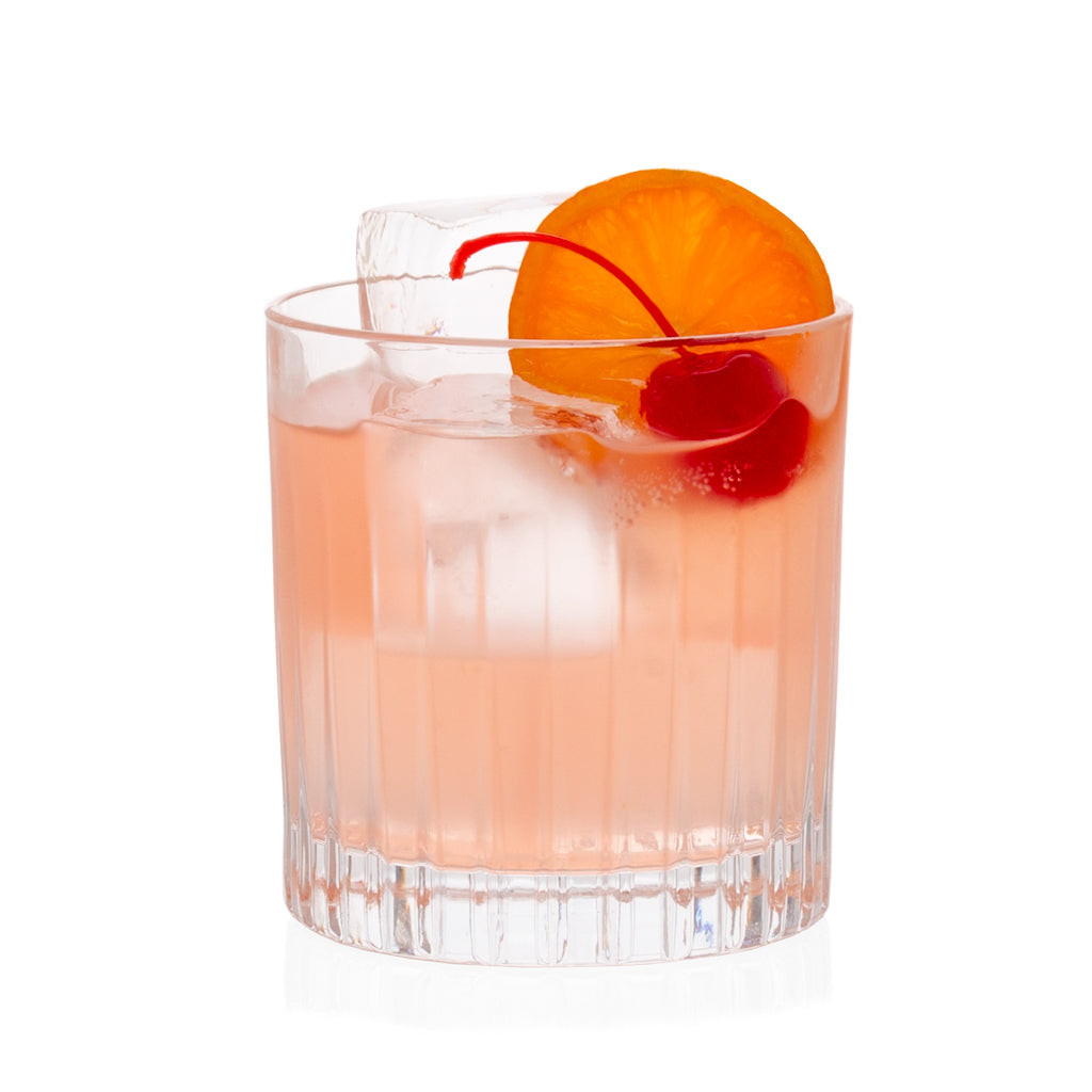 Regent Old-Fashioned glass with etched lines, holding a pink cocktail garnished with an orange slice and cherry.