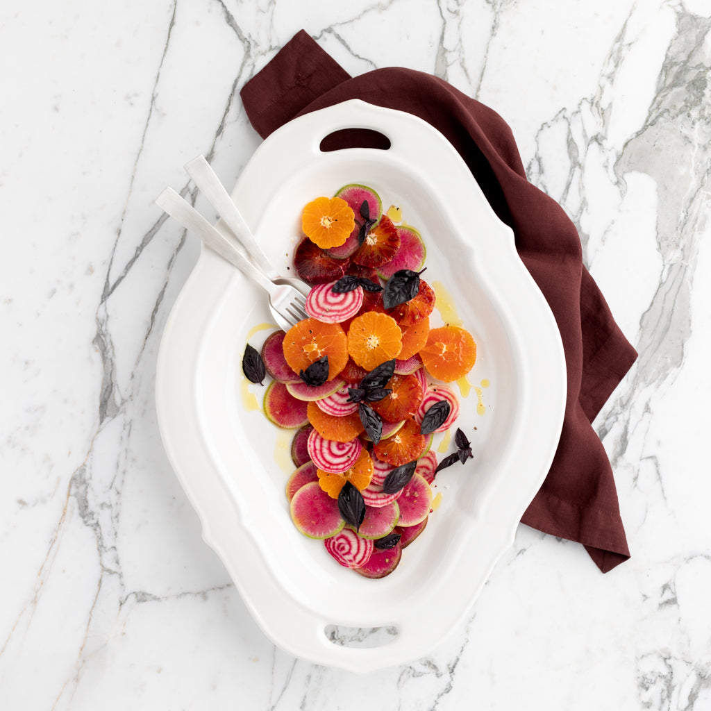 White Italian ceramic Nonna serving platter with handles, holding a colorful salad, on a marble surface.