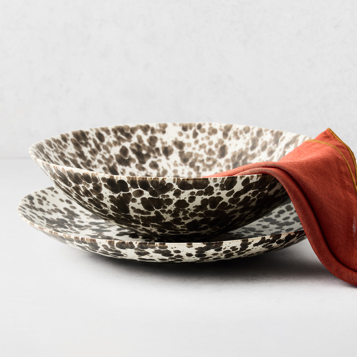 Nuno Splatter stoneware round serve platter and bowl with brown spots on cream, orange napkin.