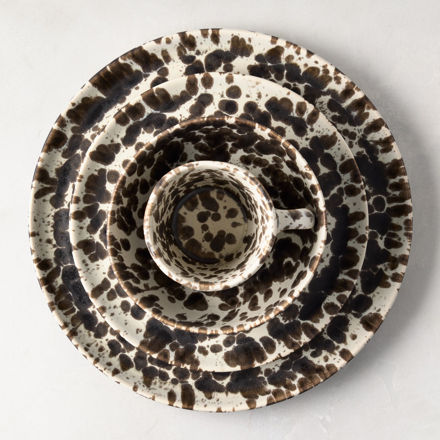 Nuno Splatter stoneware salad plate with brown spots on a pale cream base, nested with matching dinnerware.