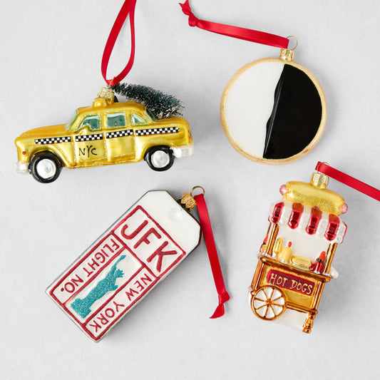 NYC-themed glass Christmas ornaments including a yellow taxi, black and white cookie, JFK luggage tag, and hot dog cart.