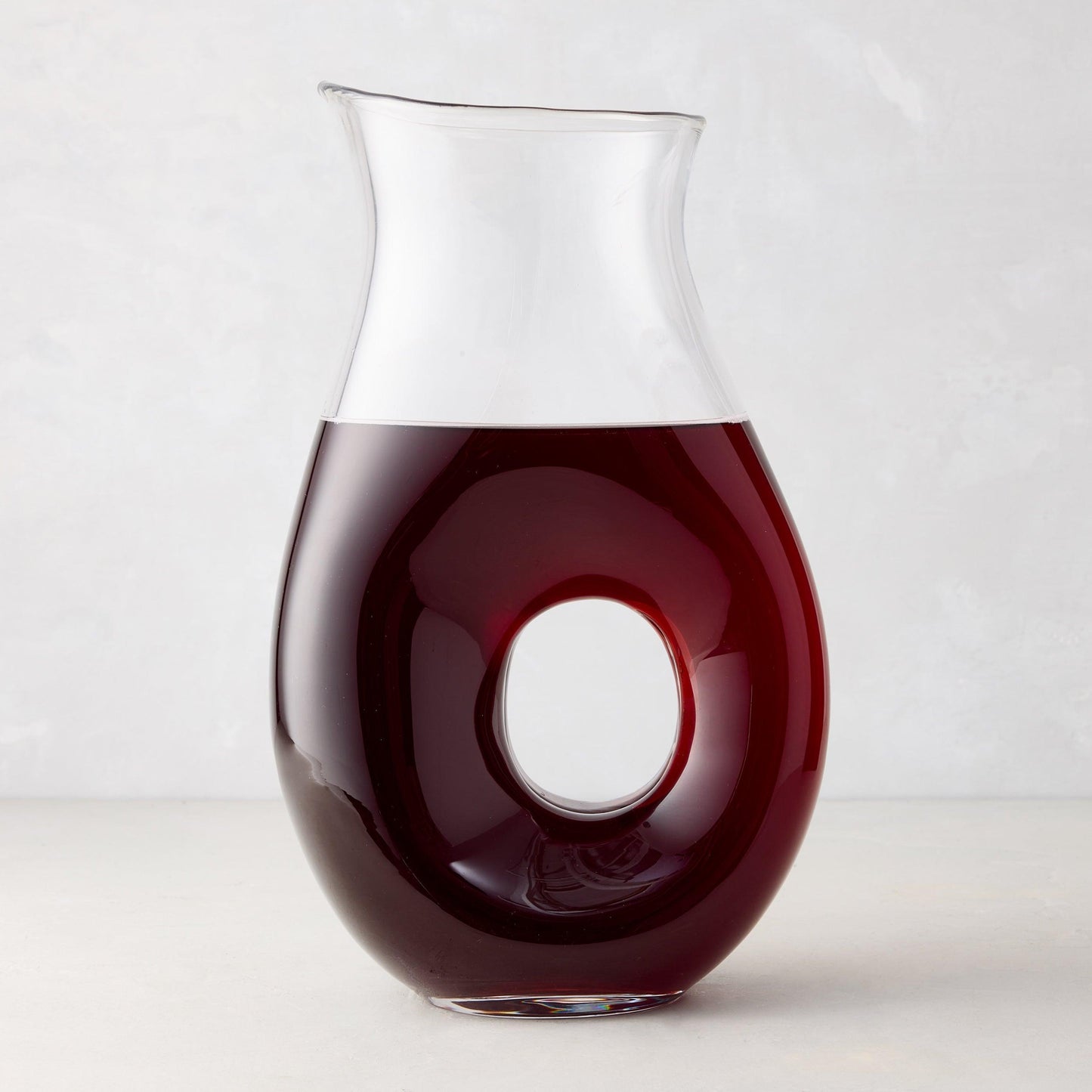 O" glass pitcher with O-shaped handle, filled with red liquid.