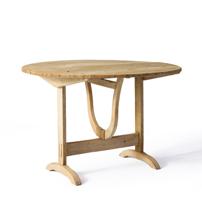 Vintage bleached oak wine tasting table with a round top and unique trestle base, featuring a rustic, worn finish.