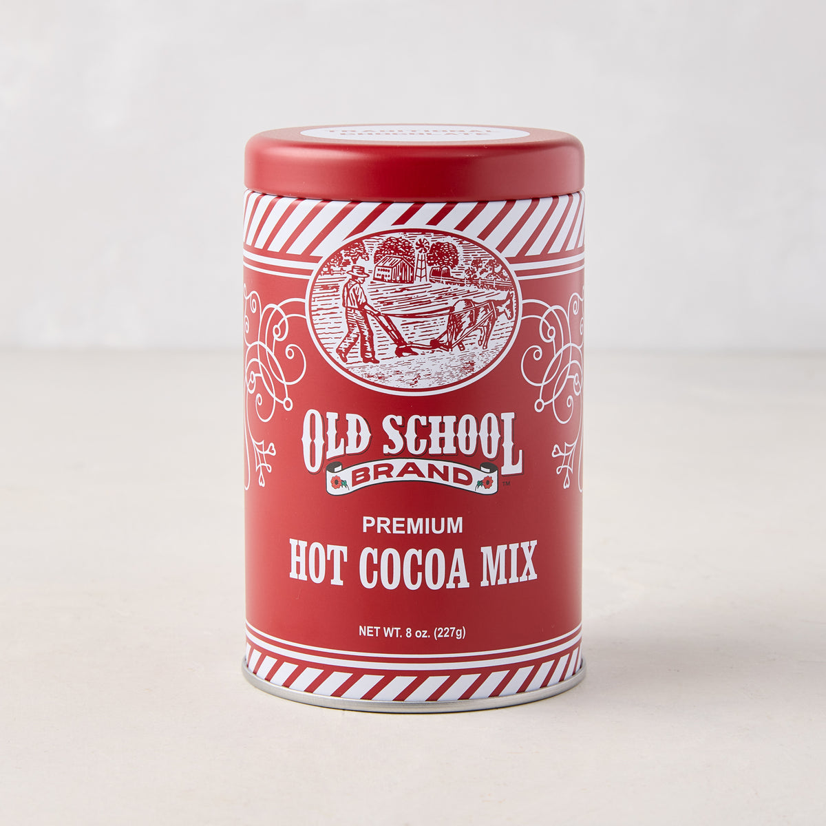 Old School Premium Hot Cocoa Mix in a red cylindrical tin with white striped borders and vintage farm illustration.