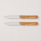Set of two Perceval 9.47 knives with stainless steel blades and polished olive wood handles on a light background.