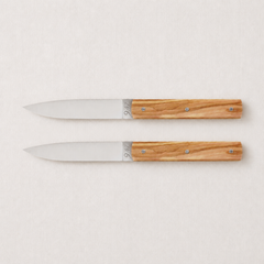 Set of two Perceval 9.47 knives with stainless steel blades and polished olive wood handles on a light background.