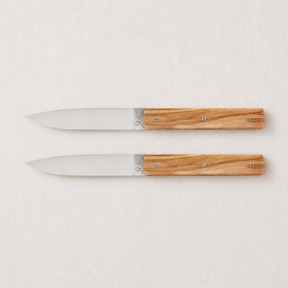 Set of two Perceval 9.47 knives with stainless steel blades and polished olive wood handles on a light background.
