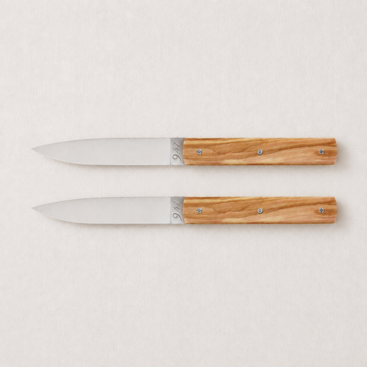 Set of two Perceval 9.47 knives with stainless steel blades and polished olive wood handles on a light background.