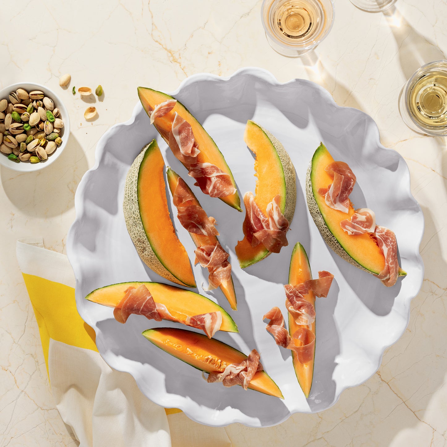 White Onda Round Ceramic Serving Platter with cantaloupe and prosciutto, pistachios, and wine.