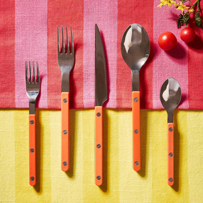 Orange 5-piece bistro flatware set with stainless steel heads and riveted acrylic handles on a striped tablecloth.
