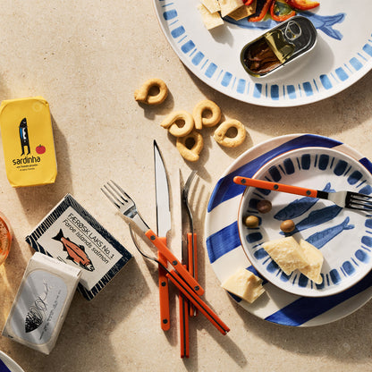 Orange 5-piece stainless steel flatware set with acrylic handles arranged on a table with plates and gourmet snacks.