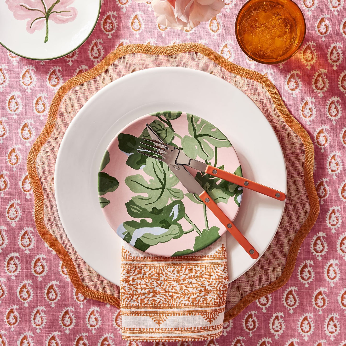 Orange bistro flatware set with stainless steel heads and vibrant orange acrylic handles on a patterned table setting.