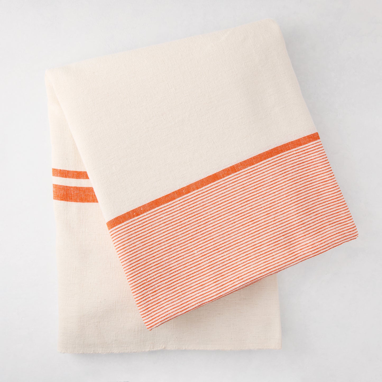 Folded Orange Boat Stripe Tablecloth, 70"x108" cotton-linen blend, with thick and thin orange stripes.