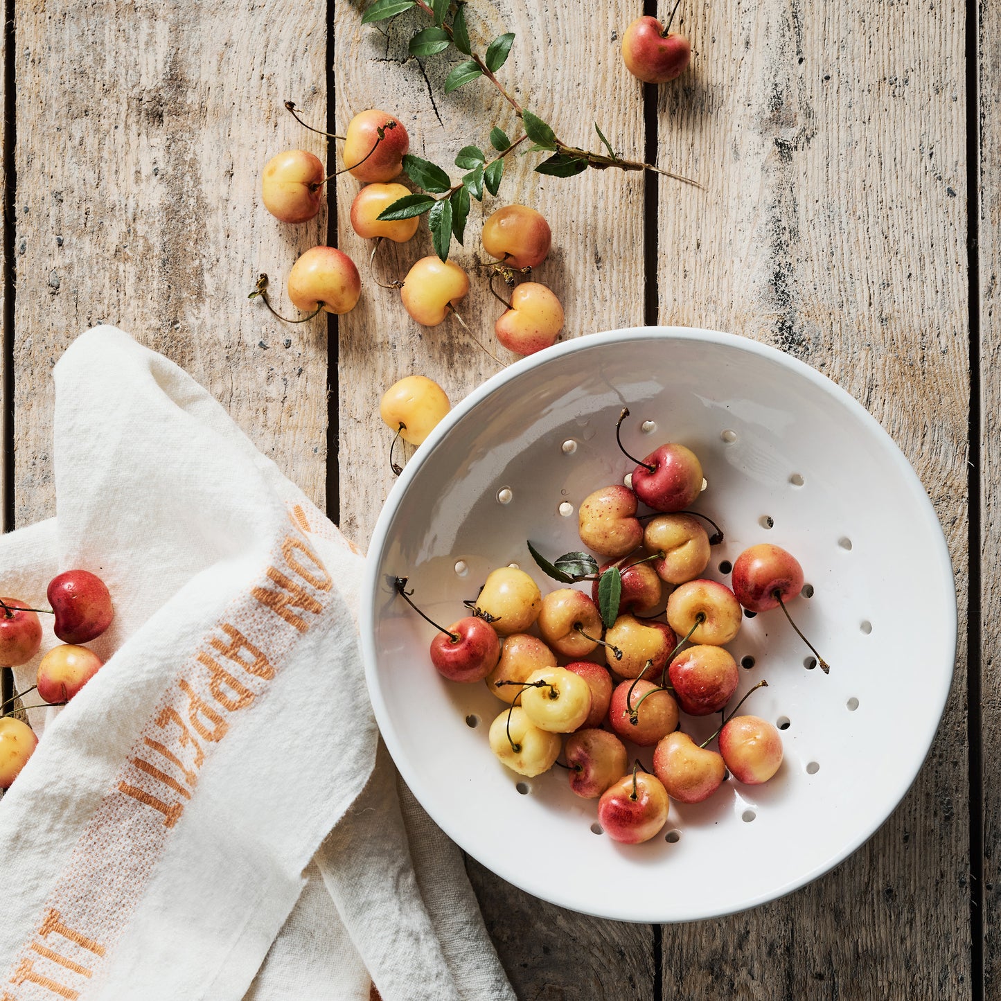 White linen hand towel with "Bon Appetit" in orange, next to a bowl of cherries on wood.