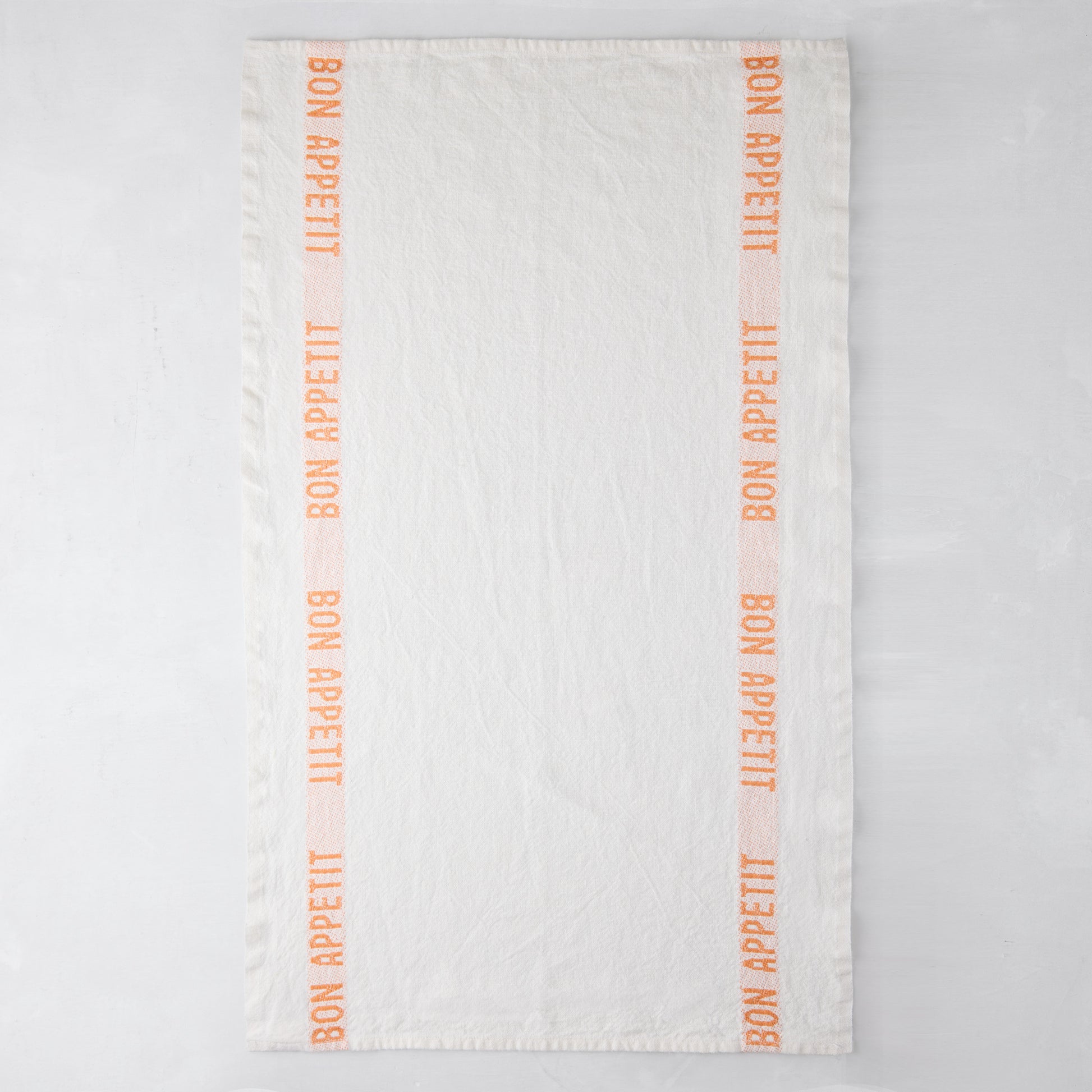White linen hand towel with orange "Bon Appetit" text stripes.