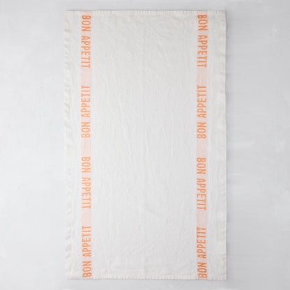 White linen hand towel with orange "Bon Appetit" text stripes.