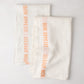 Set of 2 white linen hand towels with vertical orange "Bon Appetit" text.