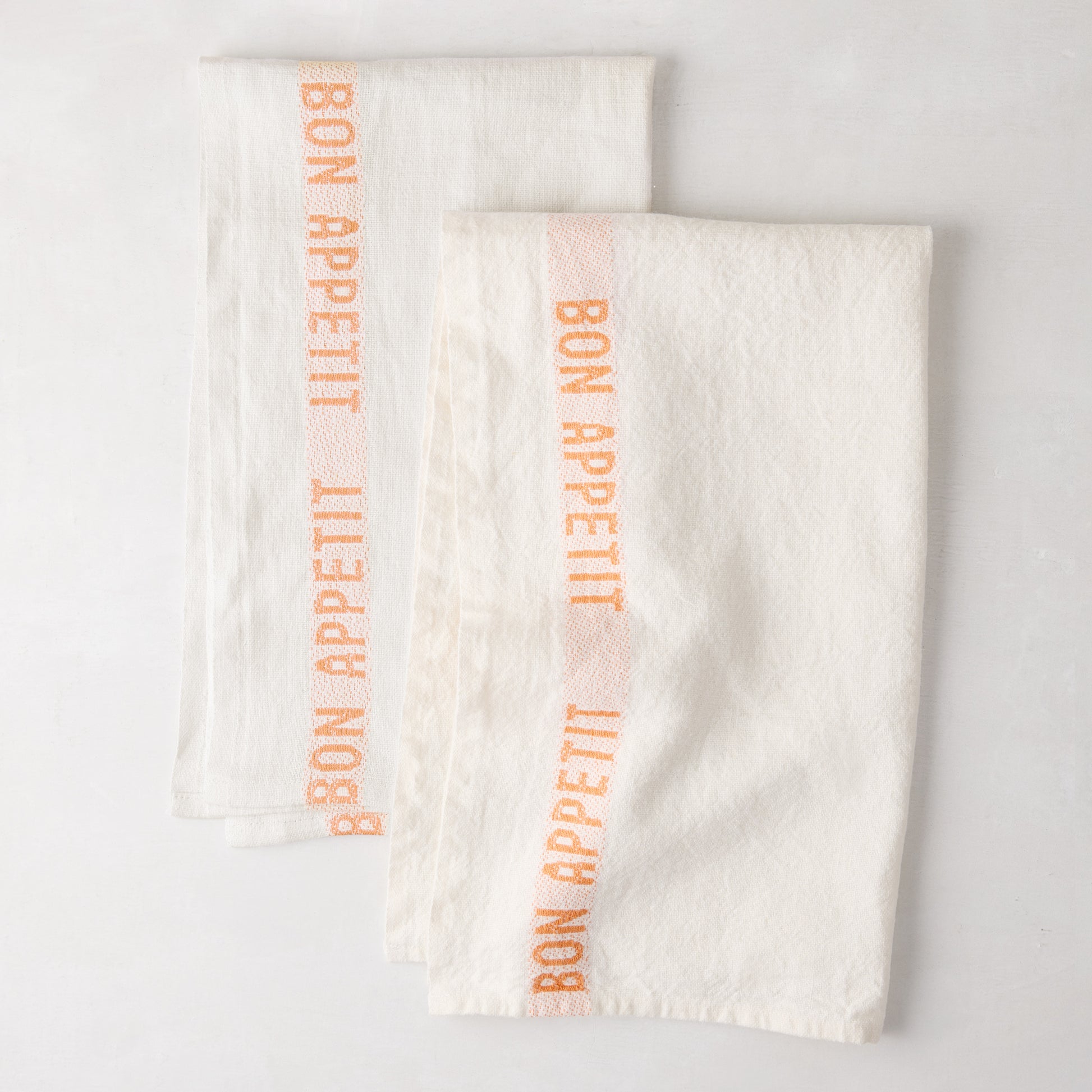 Set of 2 white linen hand towels with vertical orange "Bon Appetit" text.
