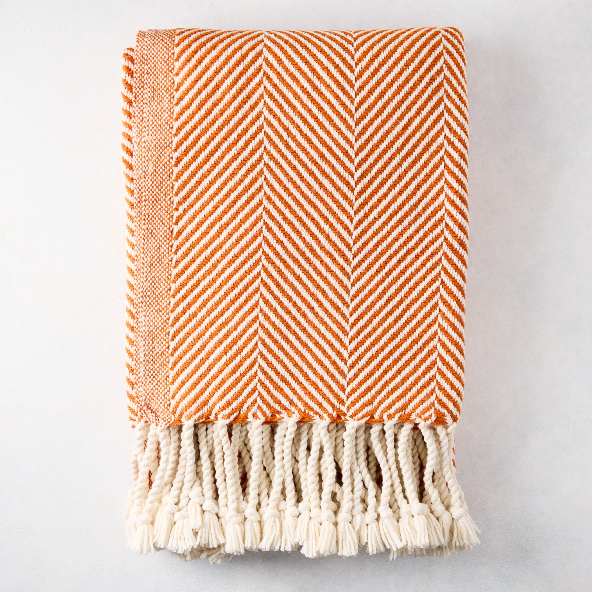 Folded orange and white chevron cotton throw blanket with thick rope fringe.