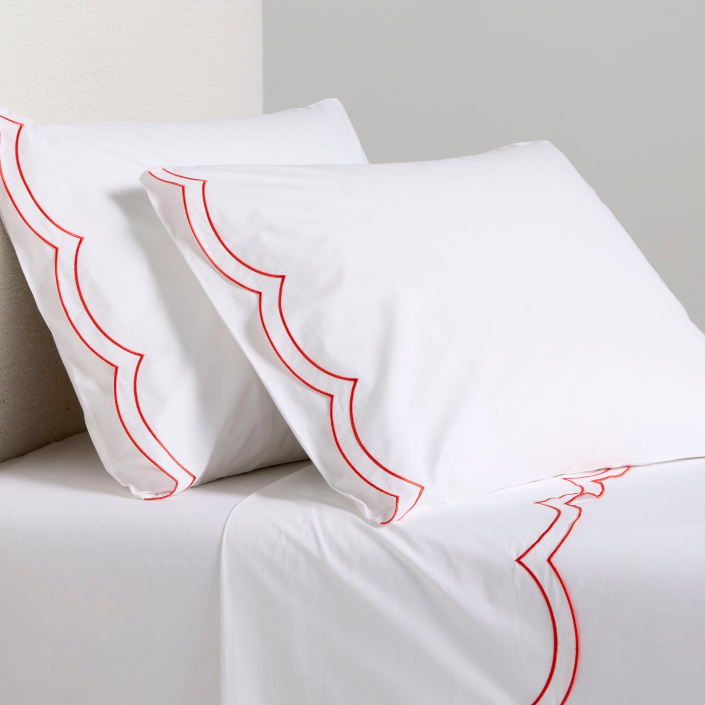 White organic cotton percale sheet set with orange double scallop stitch embroidery on pillows and flat sheet.