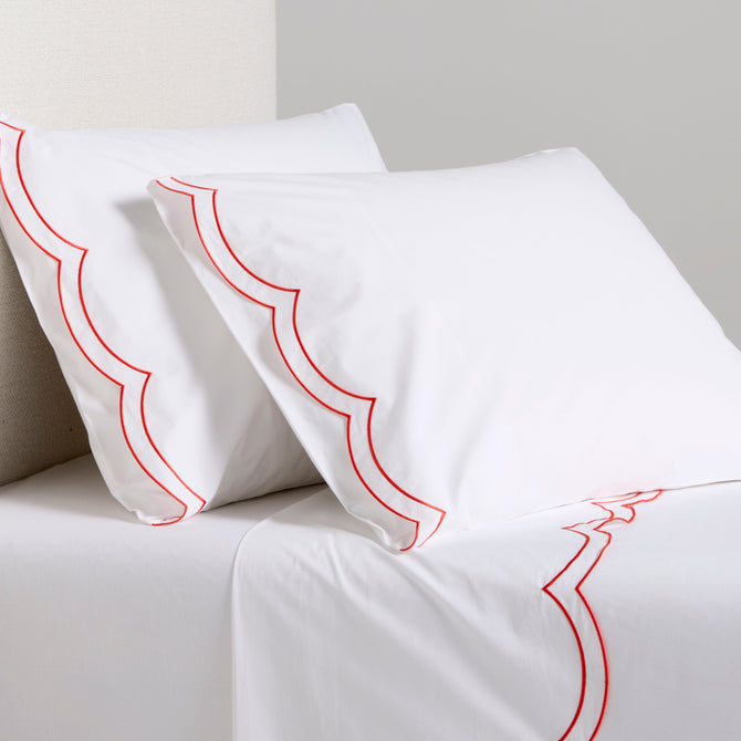 White organic cotton percale sheet set with orange double scallop stitch embroidery on pillows and flat sheet.