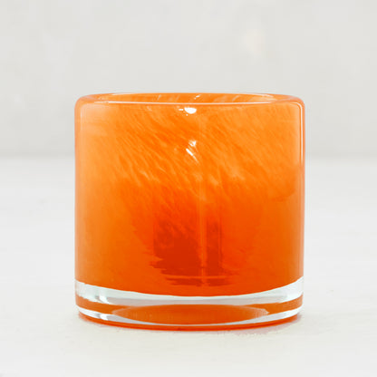 Mouth-blown, hand-formed small orange votive glass candle holder with unique swirling patterns.