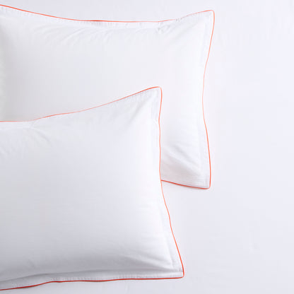 White percale pillow shams with orange piping and double-stitch detailing.