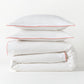 White percale duvet cover and two shams with orange piping, stacked neatly.