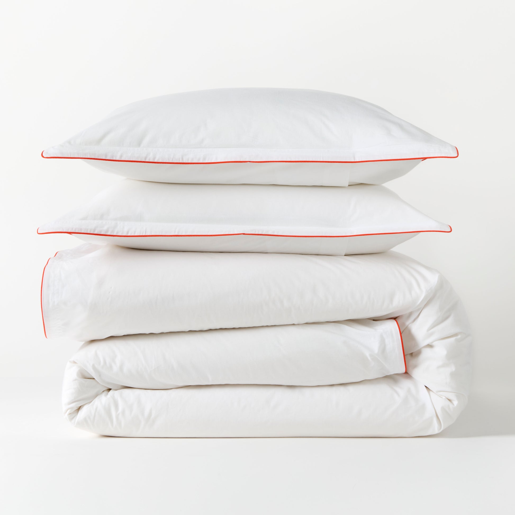White percale duvet cover and two shams with orange piping, stacked neatly.