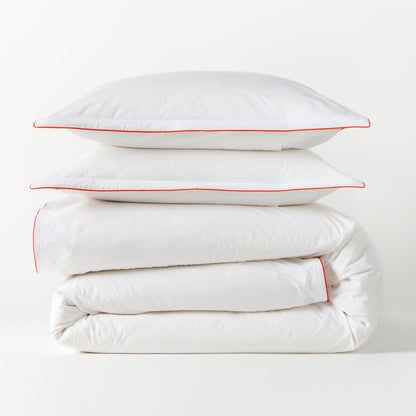 White percale duvet cover and two shams with orange piping, stacked neatly.