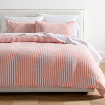 Orange seersucker stripe organic cotton duvet set with two shams on a bed.