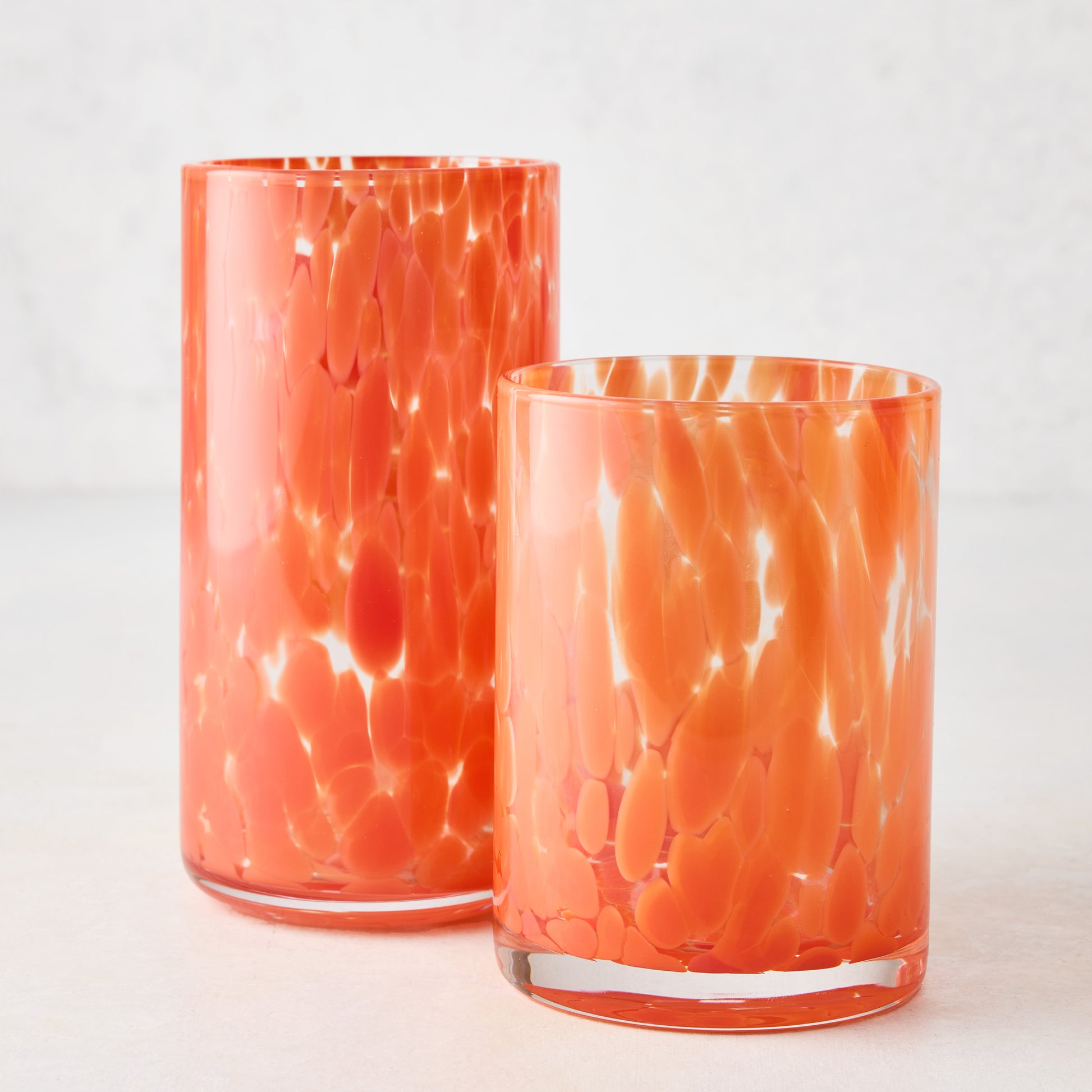 Two orange spotted highball glasses, one tall and one shorter, on a white surface.