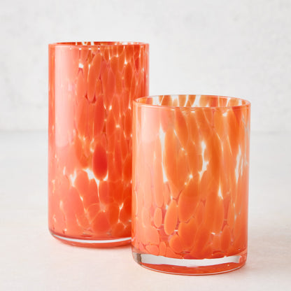 Two orange spotted highball glasses, one tall and one shorter, on a white surface.