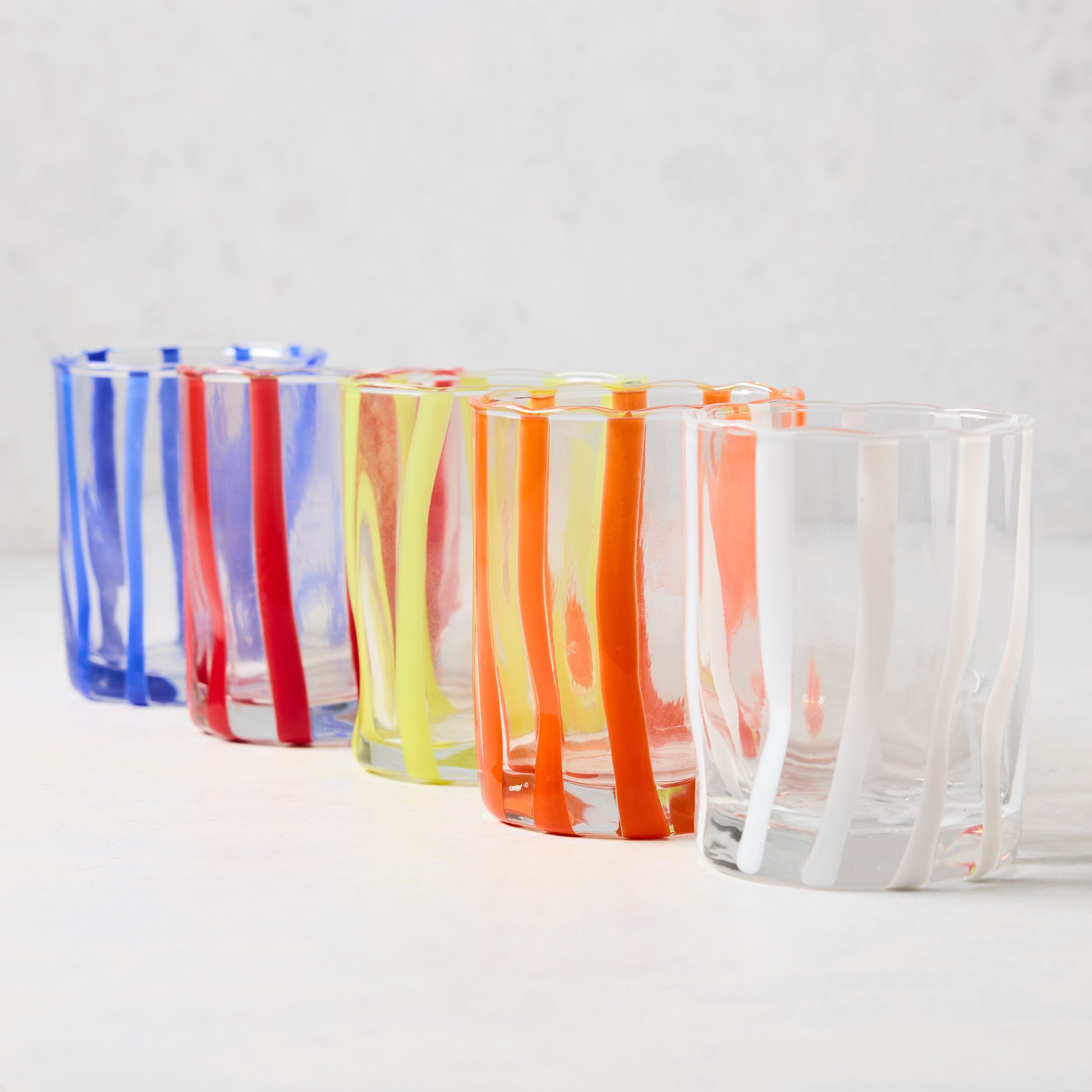 Five handmade Italian Double Old Fashioned glasses with colorful, hand-placed stripes: blue, red, yellow, orange, and white.