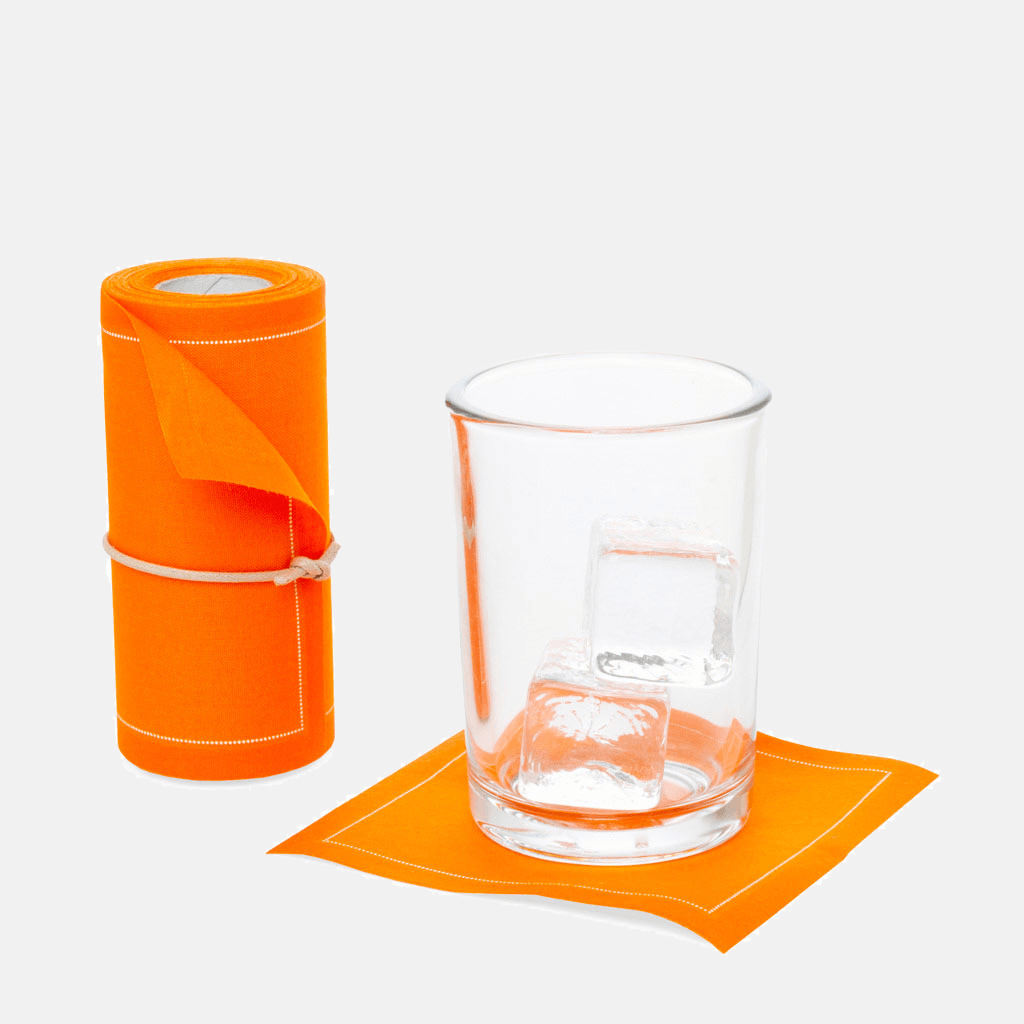 Orange tear-off cotton cocktail napkin roll with a single napkin under a glass with ice.