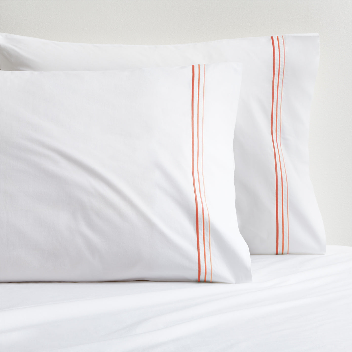 White percale pillowcases with orange ombre triple stitch embroidery.