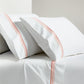 White percale sheet set with orange triple stitch embroidery on pillowcases and flat sheet.