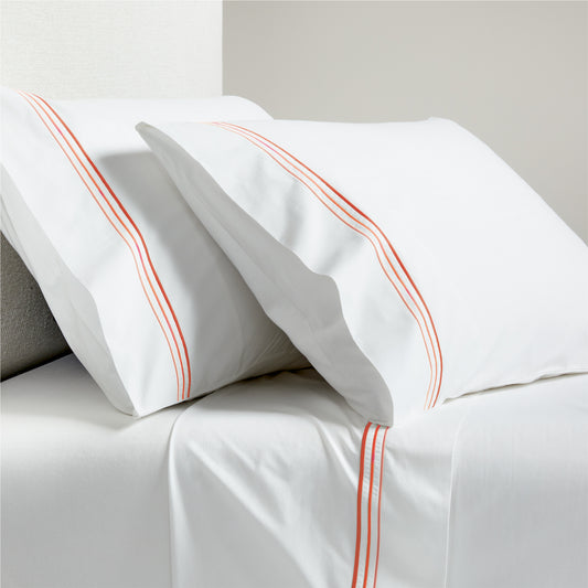 White percale sheet set with orange triple stitch embroidery on pillowcases and flat sheet.