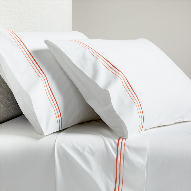 White percale sheet set with orange triple stitch embroidery on pillowcases and flat sheet.