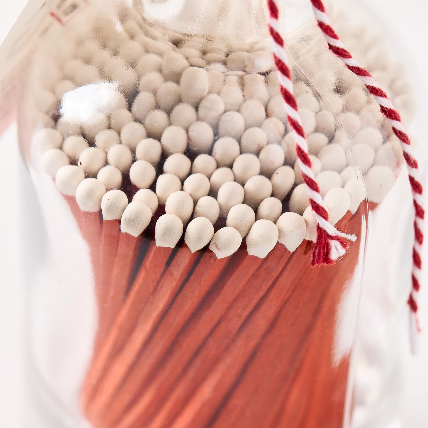 Glass bottle filled with orange matches featuring white tips, tied with red and white twine.