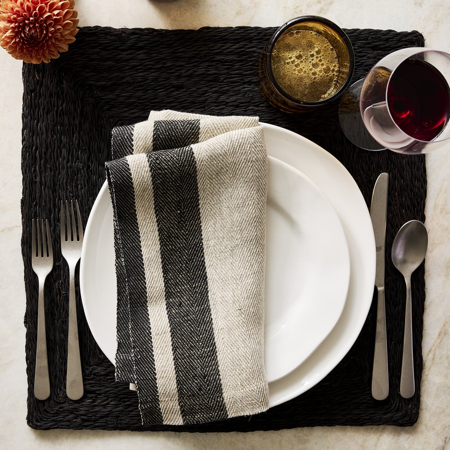 11.5-inch creamy white organic ceramic dinner plate with subtle edges on a black woven placemat with striped napkin.