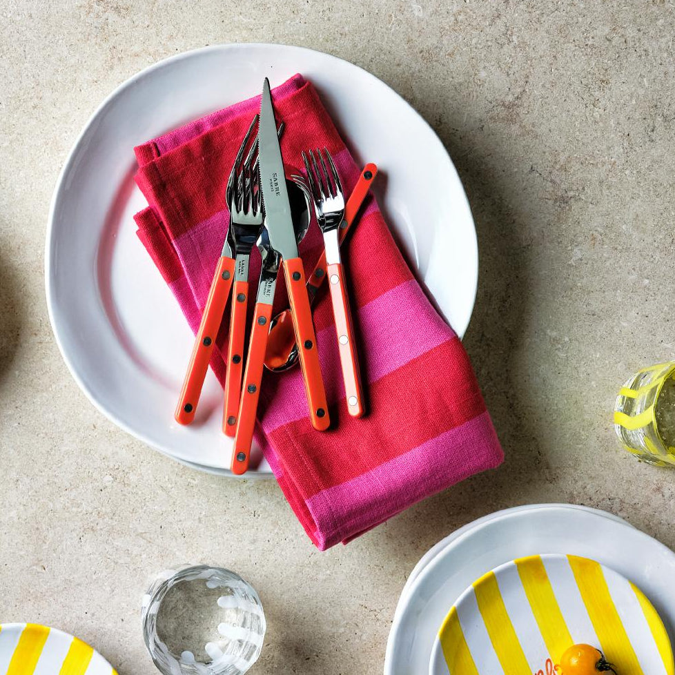 11.5-inch creamy white organic ceramic dinner plate with a pink striped napkin and orange-handled cutlery set.