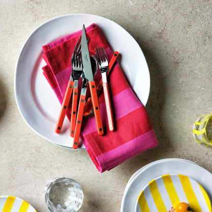 11.5-inch creamy white organic ceramic dinner plate with a pink striped napkin and orange-handled cutlery set.