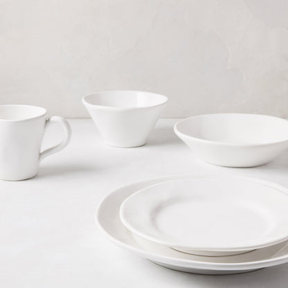 Stack of two creamy white ceramic dinner plates with subtle organic edges, a bowl, and a mug.